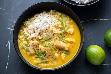 Bowl of yellow curry with fish fillet and white rice, horizontal shot on a black marble background, middle close-up