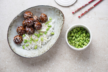 Bowl with teriyaki meatballs and white rice on a beige stone background, horizontal shot, above view