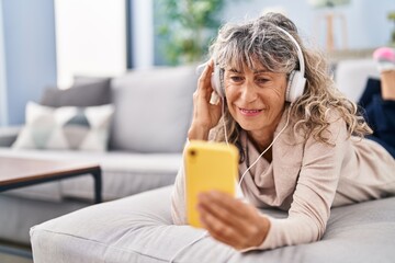 Middle age woman listening to music lying on sofa at home