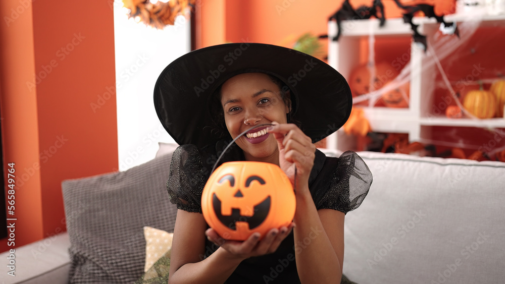 Sticker african american woman wearing witch costume holding halloween pumpkin basket at home