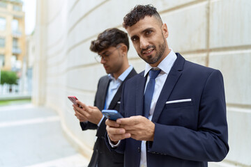 Fototapeta na wymiar Two hispanic men business workers smiling confident using smartphones at street