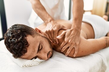 Two hispanic men physiotherapist and patient having rehab session massaging back at beauty center