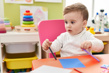 Adorable caucasian baby student sitting on table drawing on paper at kindergarten