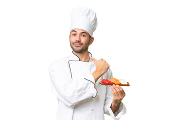 Young caucasian chef holding a sushi over isolated background proud and self-satisfied