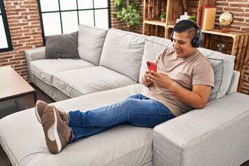 Obraz premium Young latin man listening to music sitting on sofa at home