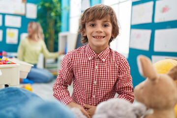 Adorable caucasian boy student smiling confident sitting on floor at kindergarten