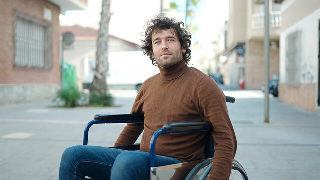 Young Hispanic Man Sitting On Wheelchair With Relaxed Expression At Street