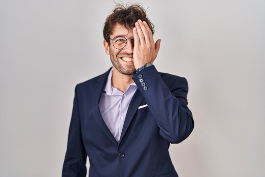 Hispanic business man wearing glasses covering one eye with hand, confident smile on face and surprise emotion.
