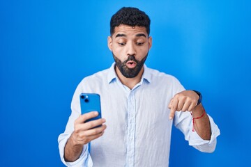Hispanic man with beard using smartphone typing message pointing down with fingers showing advertisement, surprised face and open mouth © Krakenimages.com