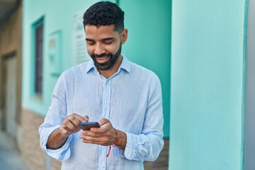 Young arab man smiling confident using smartphone at street