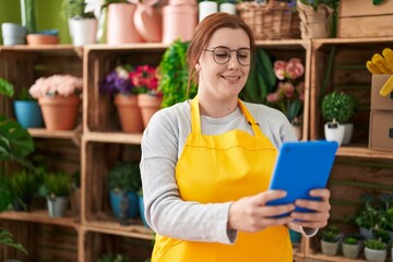 Young beautiful plus size woman florist smiling confident using touchpad at flower shop