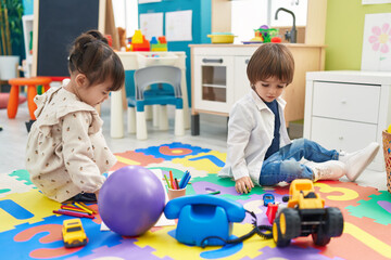 Two kids playing with toys sitting on floor at kindergarten