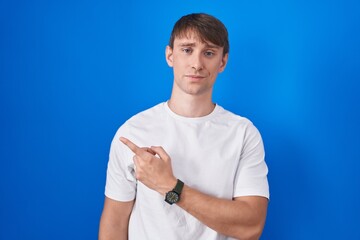 Caucasian blond man standing over blue background pointing aside worried and nervous with...