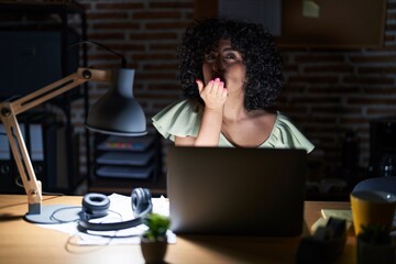 Young brunette woman with curly hair working at the office at night looking at the camera blowing a kiss with hand on air being lovely and sexy. love expression.