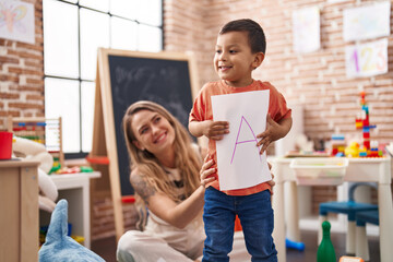 Teacher and toddler holding paper standing at kindergarten