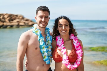 Young hispanic couple tourists wearing hawaiian lei hugging each other at seaside