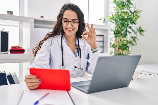 Young doctor woman working on online appointment doing ok sign with fingers, smiling friendly gesturing excellent symbol
