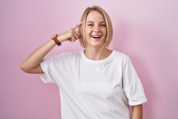 Young caucasian woman standing over pink background smiling pointing to head with one finger, great idea or thought, good memory