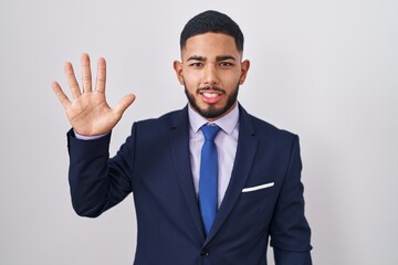 Young hispanic man wearing business suit and tie showing and pointing up with fingers number five while smiling confident and happy.