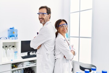 Middle age man and woman partners wearing scientist uniform standing with arms crossed gesture at laboratory