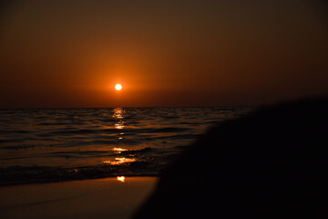 Vibrant sunset descending on the horizon, sea in golden colors, small waves gently touching the...