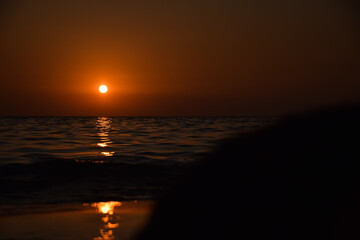 Vibrant sunset descending on the horizon, sea in golden colors, small waves gently touching the...