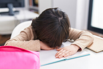 Adorable hispanic girl student stressed leaning on book at classroom