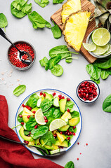 Fresh salad with pineapple, spinach, avocado and pomegranate on gray kitchen table, top view. Healthy vegan eating, clean food, diet, weight loss dish