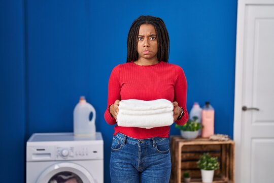 Young african american with braids holding clean laundry depressed and worry for distress, crying angry and afraid. sad expression.