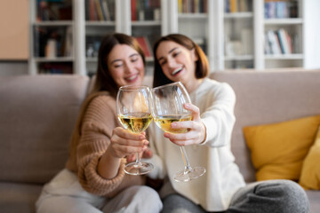 Cheerful pretty european millennial women in sweaters cheers glasses of wine, enjoy relax and free time