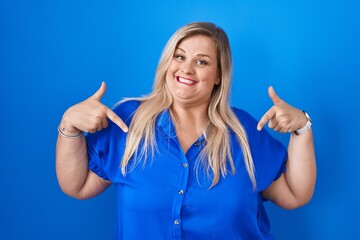 Caucasian plus size woman standing over blue background looking confident with smile on face,...