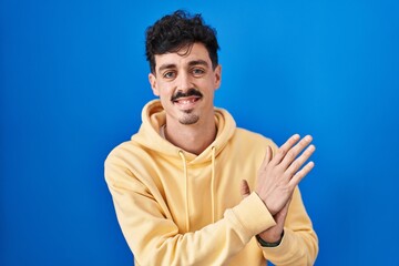 Hispanic man standing over blue background clapping and applauding happy and joyful, smiling proud hands together