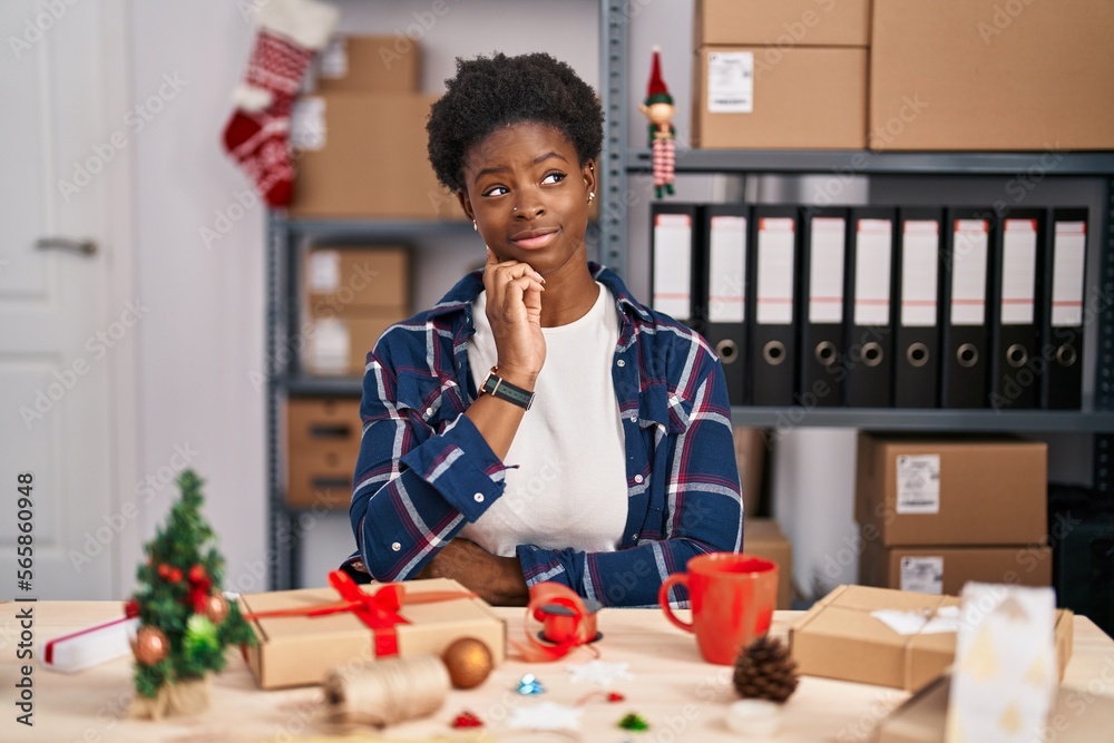 Sticker African american woman working at small business doing christmas decoration with hand on chin thinking about question, pensive expression. smiling with thoughtful face. doubt concept.