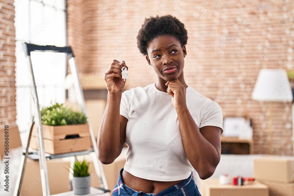 Sticker African american woman holding keys of new home serious face thinking about question with hand on chin, thoughtful about confusing idea