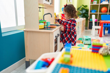 Adorable blonde toddler playing with play kitchen standing at kindergarten