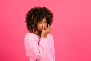 Sad dissatisfied upset young black curly lady in casual covering nose with hand, looking at camera