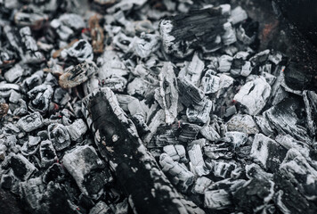 Photo of smoldering gray coals, burnt ash close-up in a fire.