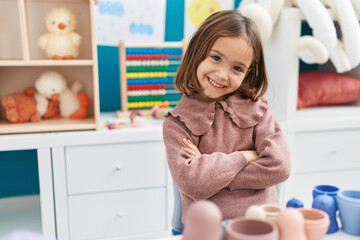 Adorable hispanic girl smiling confident sitting on table with arms crossed gesture at kindergarten