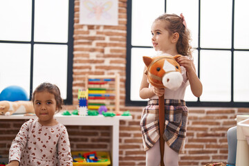 Two kids playing with horse toy at kindergarten