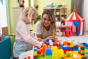 Teacher and toddler playing with construction blocks sitting on table at kindergarten