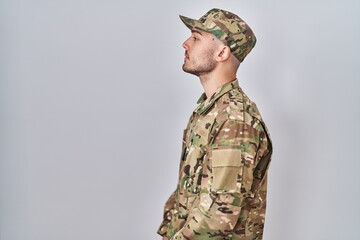 Young hispanic man wearing camouflage army uniform looking to side, relax profile pose with natural...