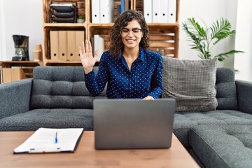 Young brunette woman working at psychology clinic doing online appointment looking positive and happy standing and smiling with a confident smile showing teeth