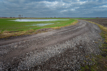 Gravel road in farmland and cloudy sky in eastern Poland