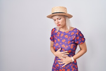 Young caucasian woman wearing flowers dress and summer hat with hand on stomach because...