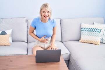 Young blonde woman watching movie on laptop at home