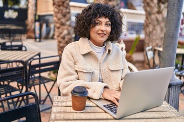 Fototapeta na wymiar Young beautiful hispanic woman using laptop sitting on table at coffee shop terrace