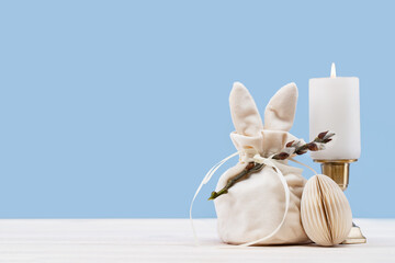 Easter bunny shaped Ivory gift bag with sweets candle and paper craft Easter egg on white wooden table, blue background banner. Willow branch