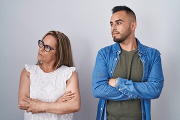 Hispanic mother and son standing together looking to the side with arms crossed convinced and confident