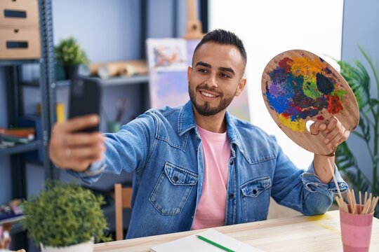 Young hispanic man artist make selfie by smartphone holding palette at art studio