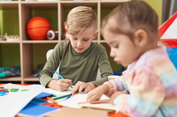 Fototapeta premium Two kids preschool students sitting on table drawing on paper at kindergarten